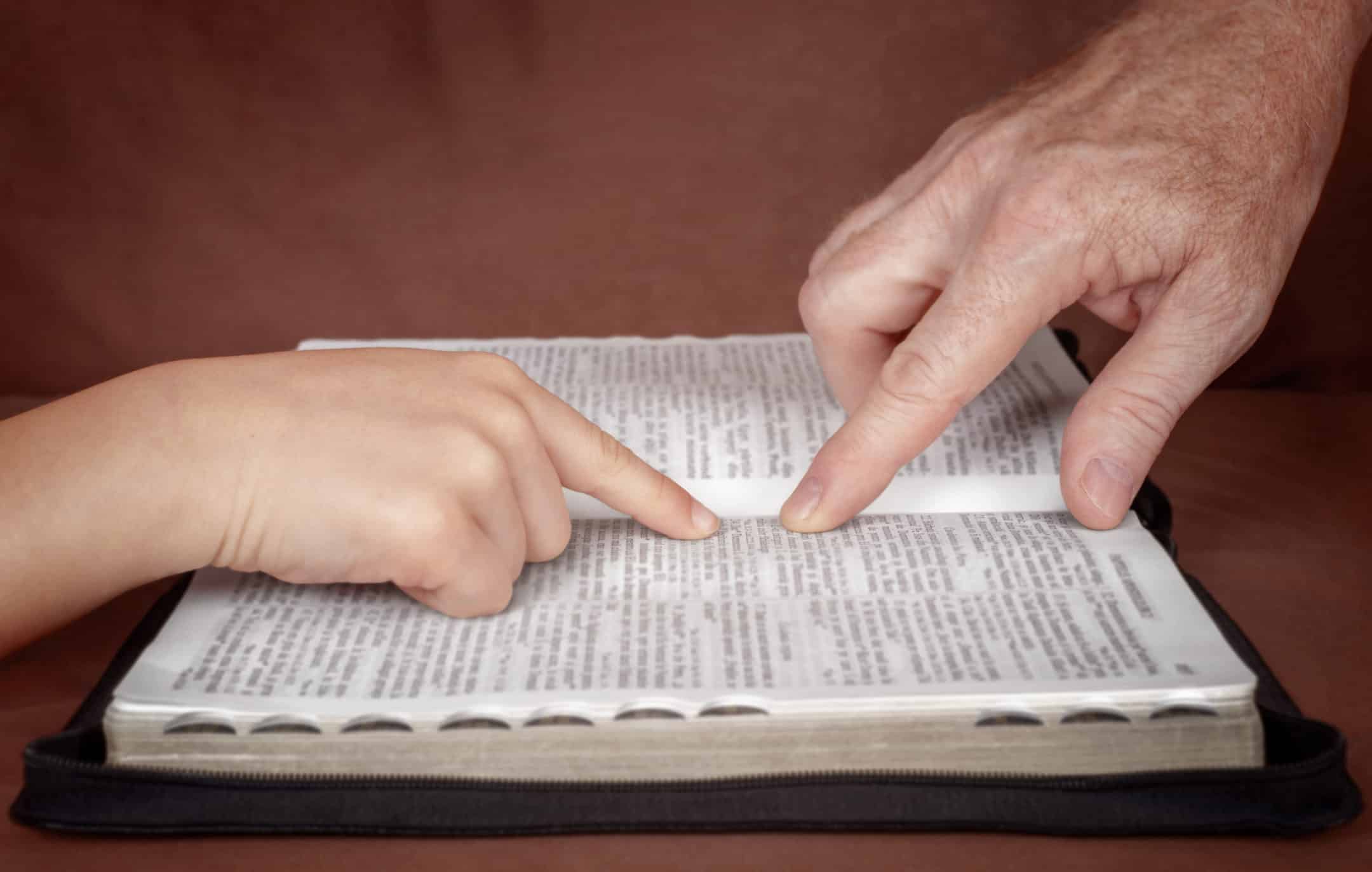 adult pointing something from the bible to a child