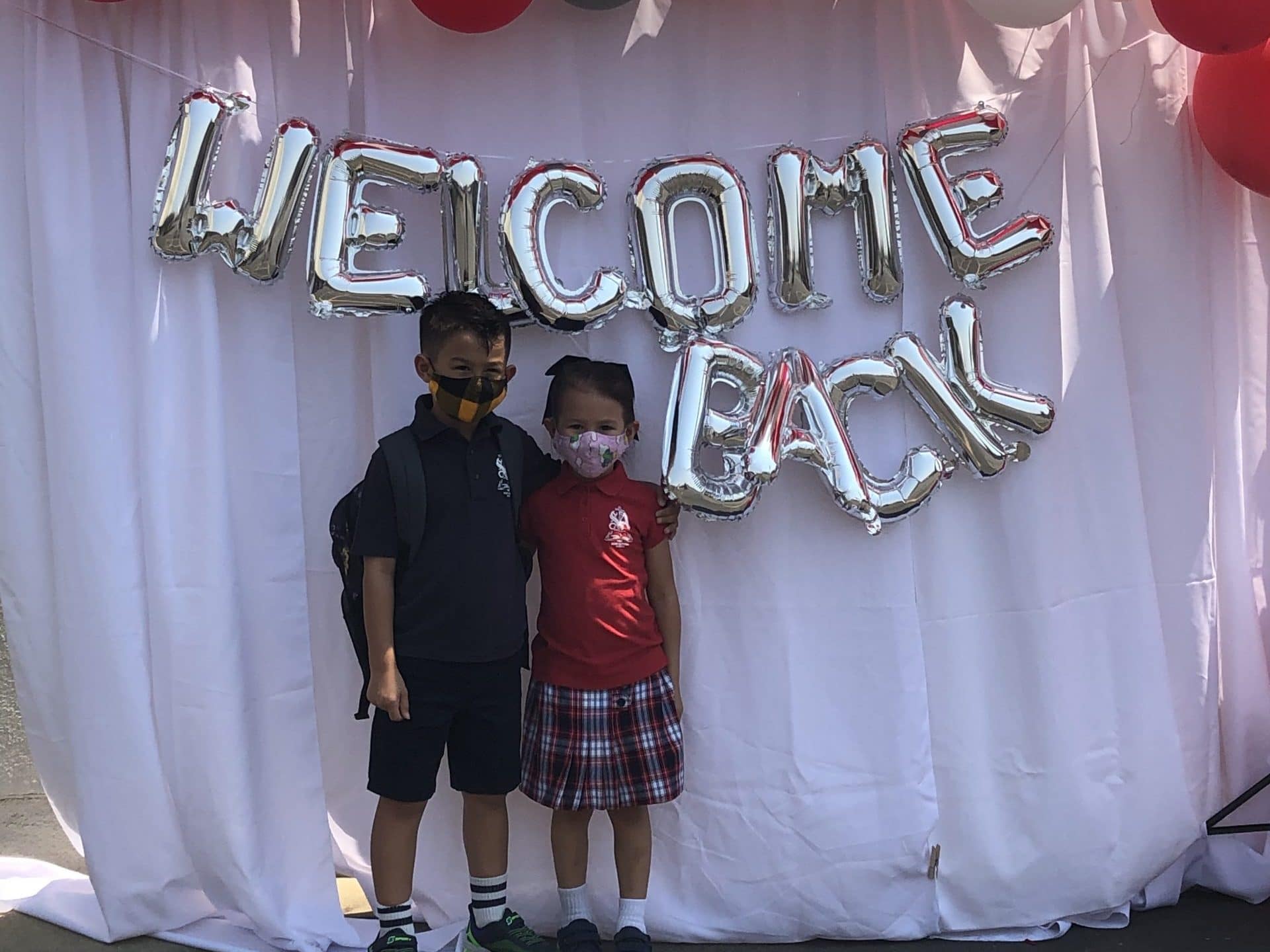 two students stand by a 'Welcome Back' sign indicating the return to school