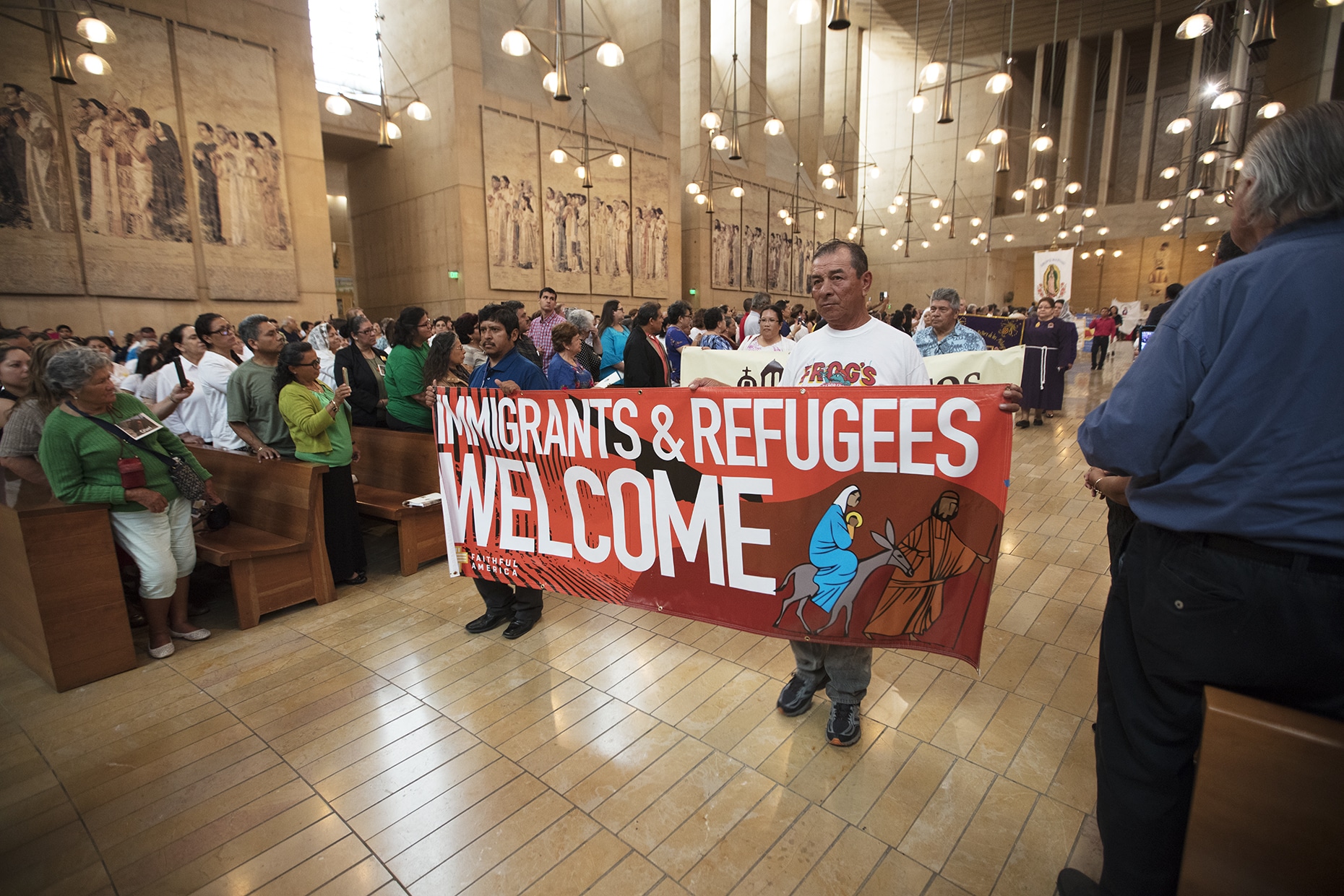 procession for Immigration Mass. Men holding up banner that says 'Immigrants and Refugees Welcome"