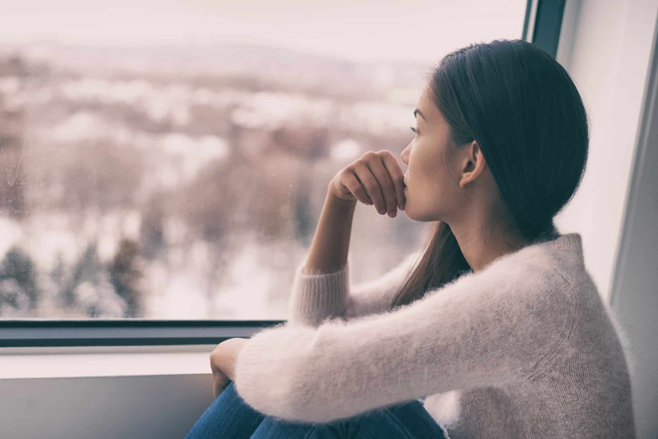 Sad pensive woman sitting by the window