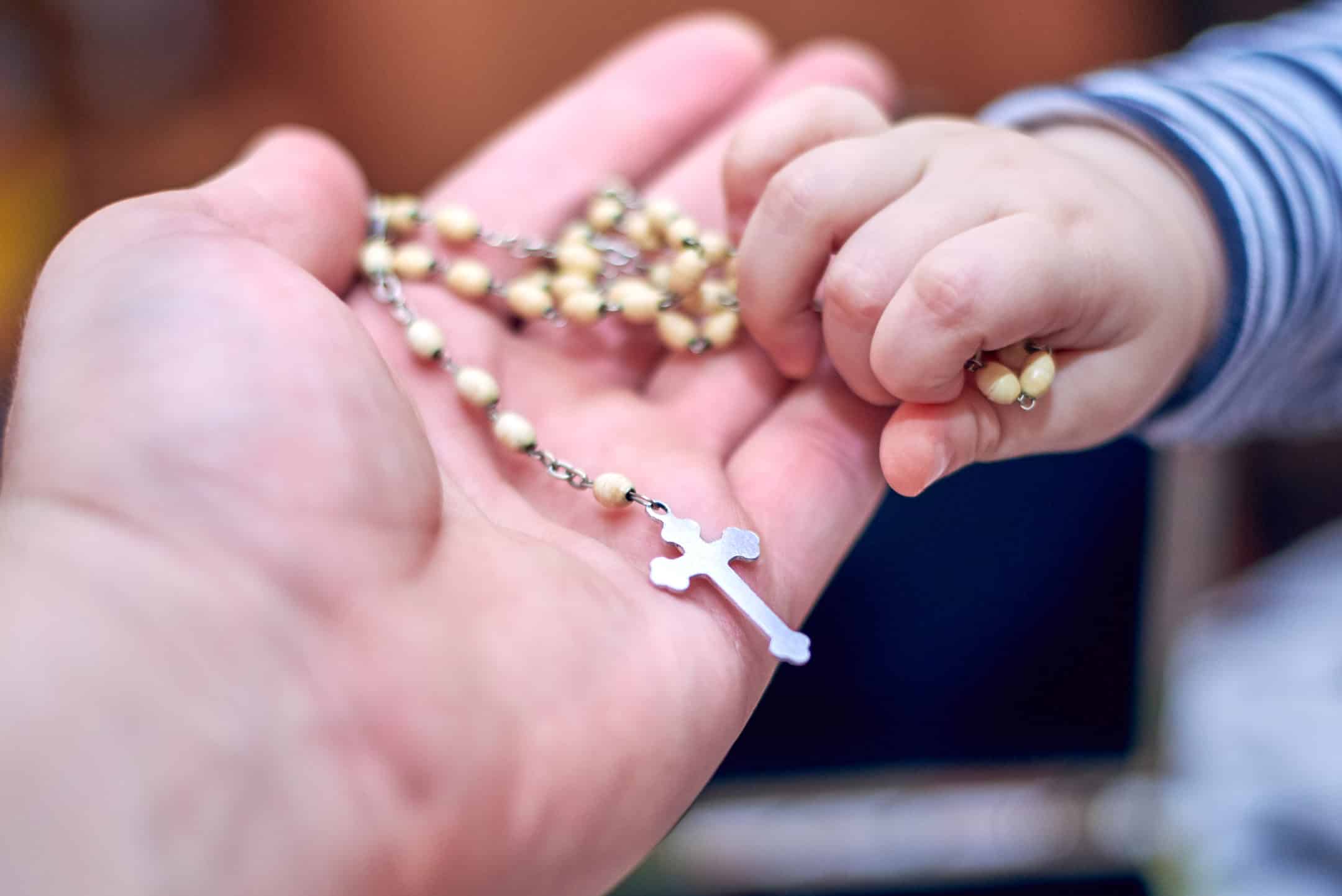 small child hand taking a rosary from his dad's hand