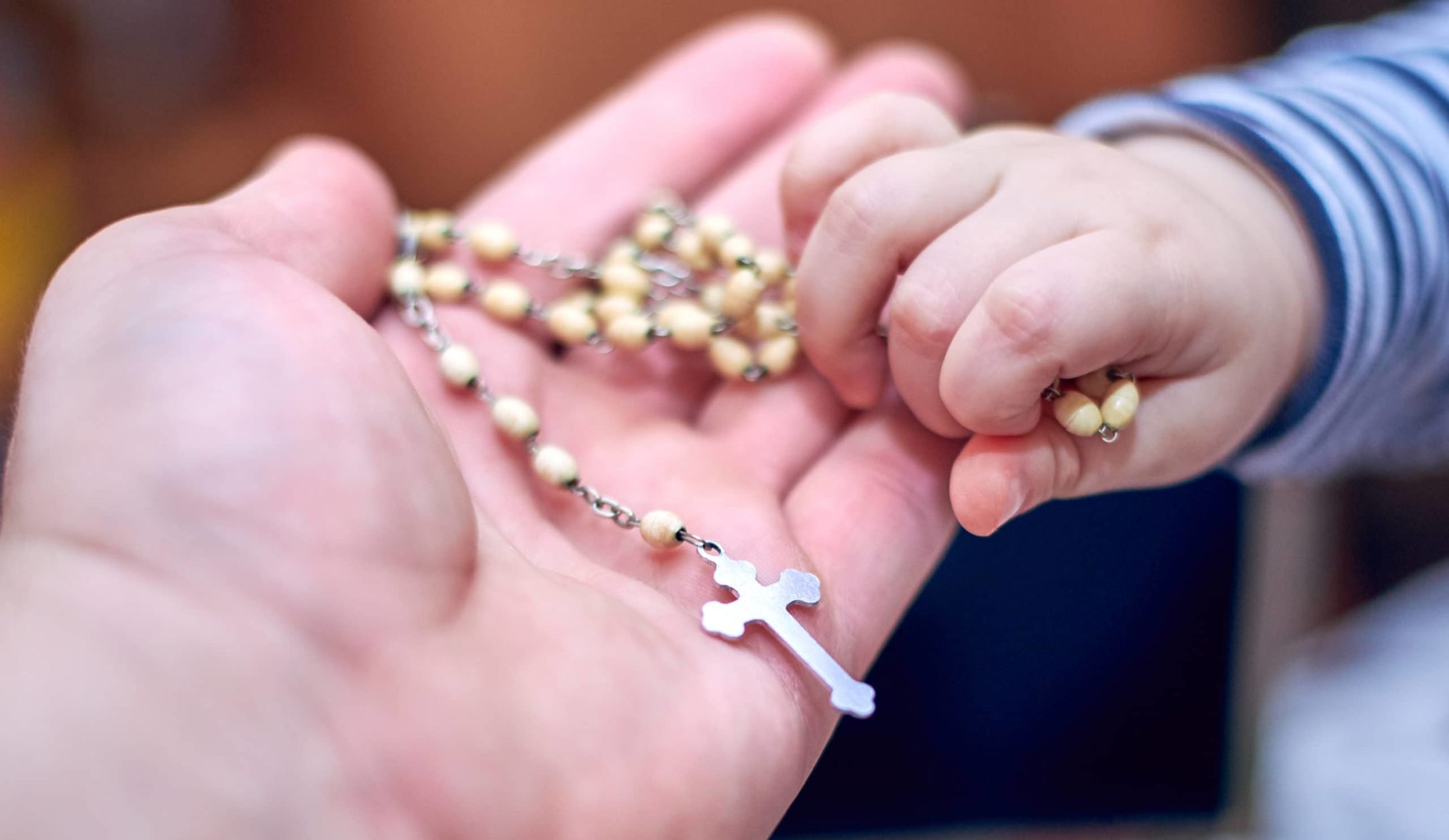 small child hand taking a rosary from his dad's hand