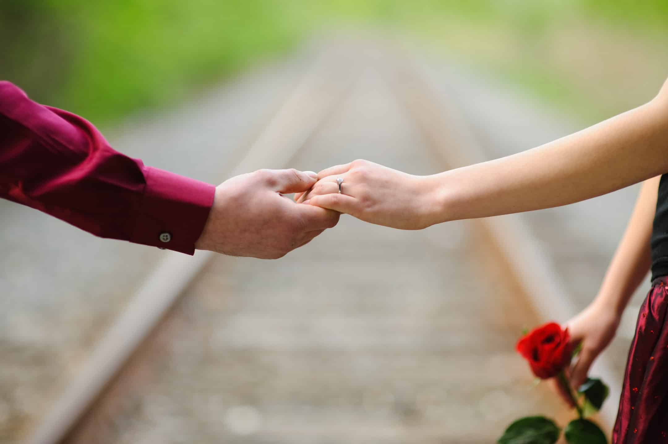 Engaged couple holding hands near train tracks