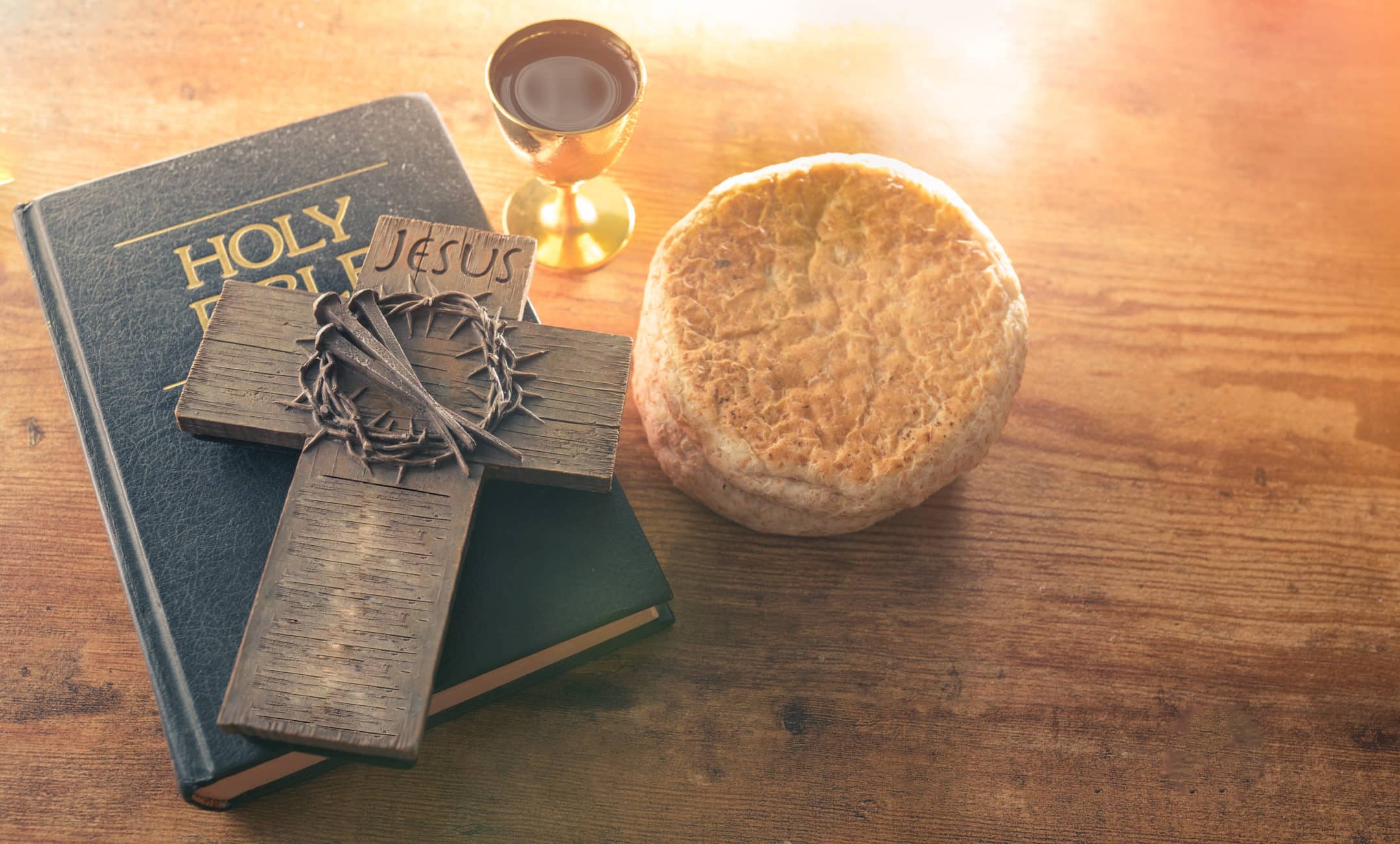 Cup of glass with red wine, bread and Holy Bible and Cross on wooden table.