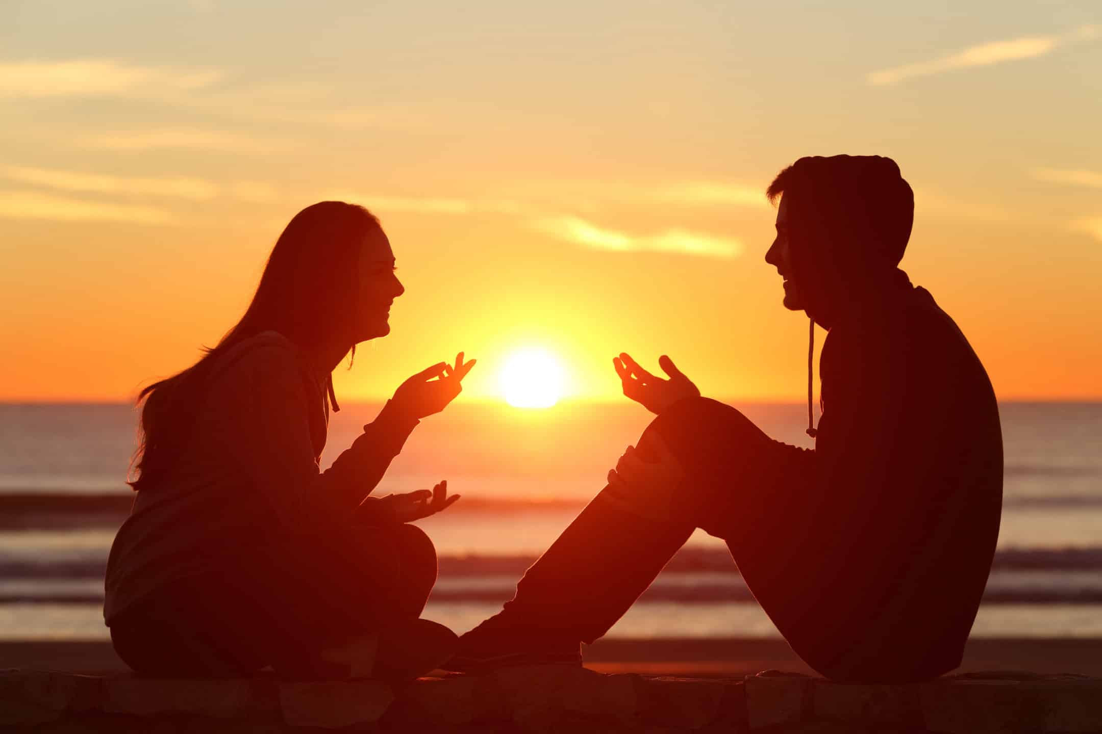 two friends sitting and talking at sunrise on the beach