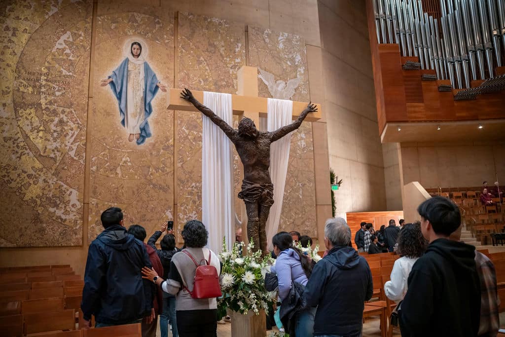 Crucifix centerpiece with statue of Jesus and white drapery in a church, surrounded by worshippers.