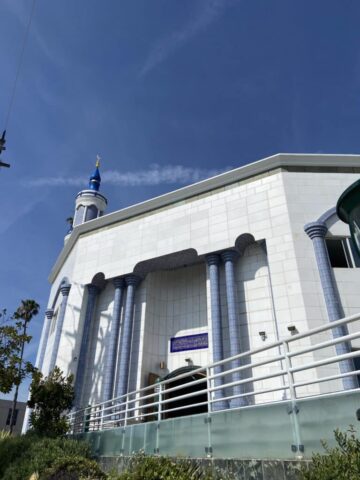 White mosque-style building with a blue minaret dome and gold crescent against a clear blue sky?