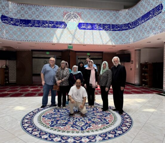 Group of adults posing for a photo in a lobby with blue geometric tile walls and a large circular patterned rug.