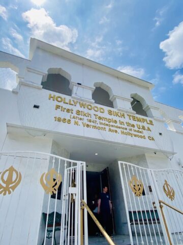 Entrance to the Hollywood Sikh Temple, a white building with arched openings and gold lettering on the facade against a blue sky.