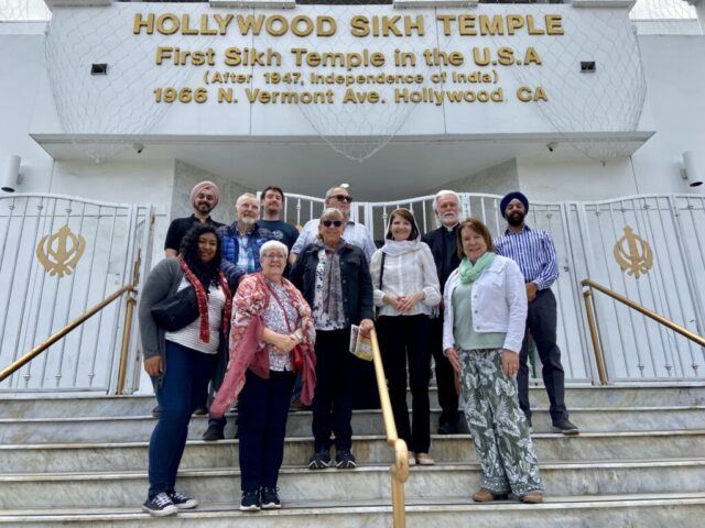 Group photo of diverse adults standing on marble steps in front of the Hollywood Sikh Temple entrance.