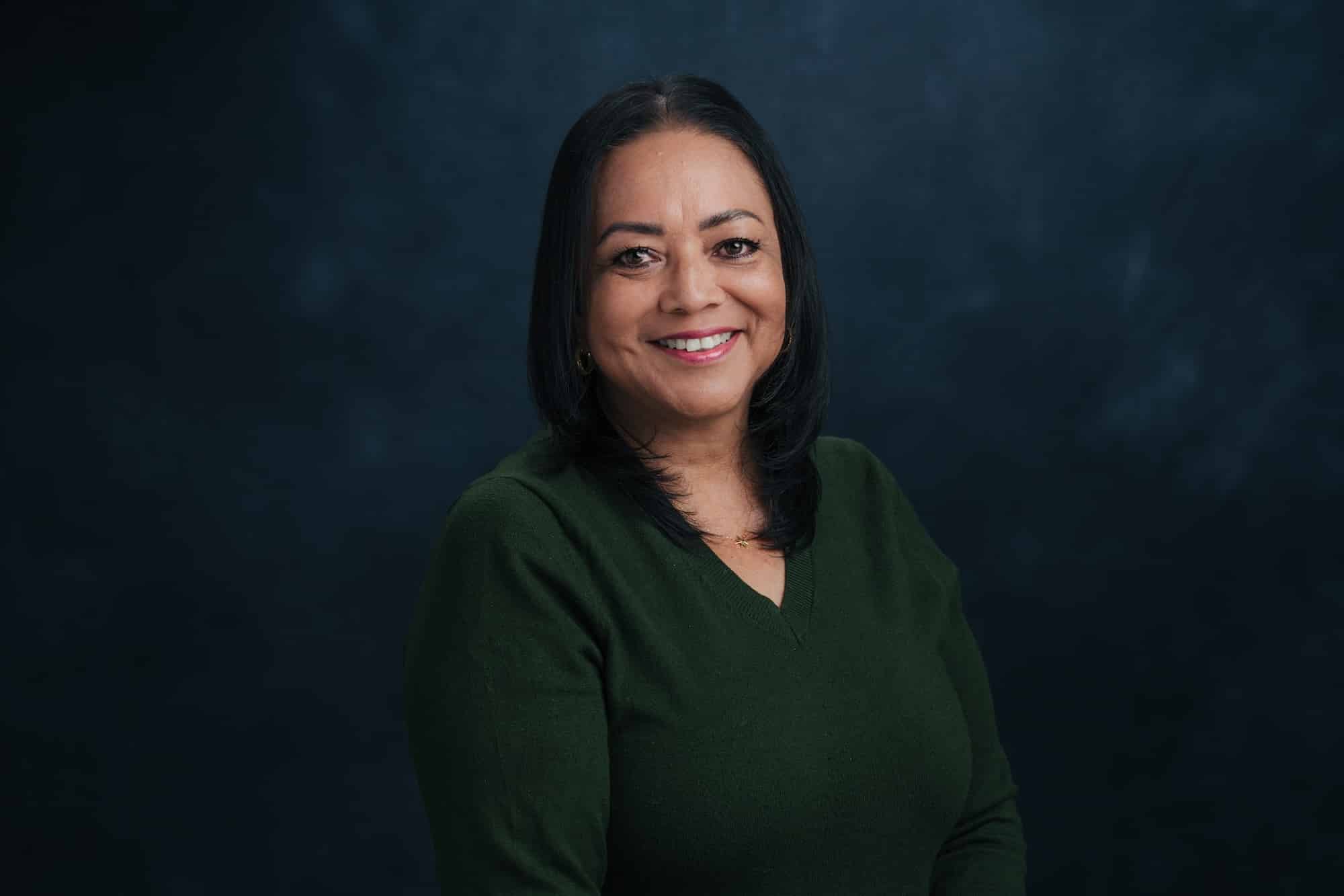 Smiling woman with dark hair in a green sweater against a dark blue backdrop.
