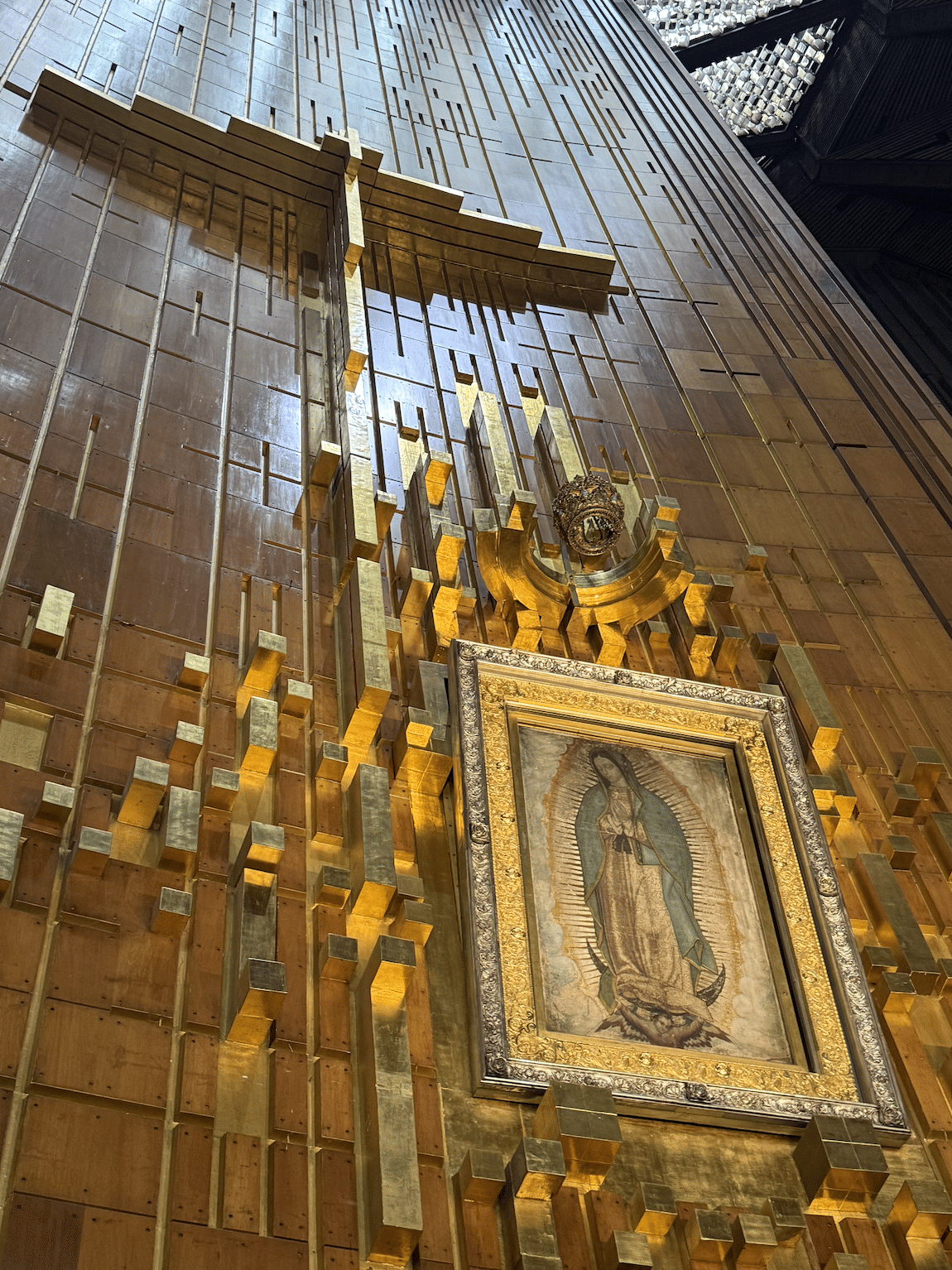 Framed image of the Virgin Mary mounted on a gold, geometric altar wall with stepped gold blocks around it.